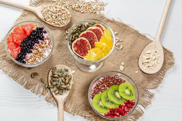 Three bowls of oatmeal with fresh fruit and seeds on a burlap background with wooden spoons