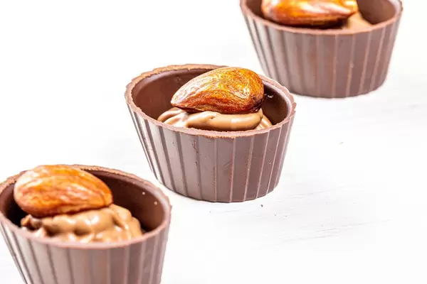 Three chocolates with whole almonds on white wooden background