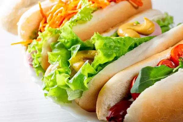 Three fresh hot dogs with vegetables, sausages and greens close-up
