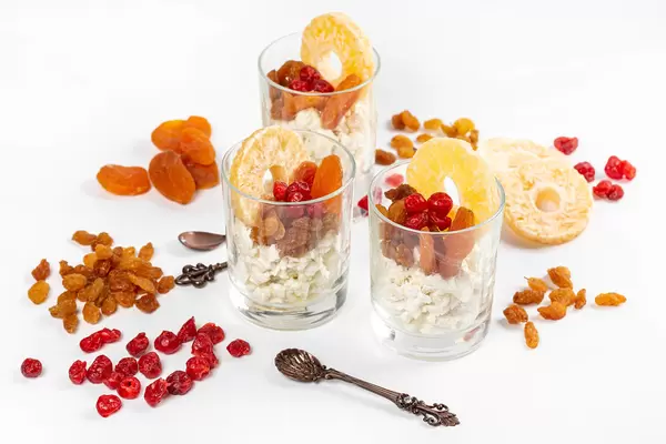 Three glasses with cottage cheese and dried fruits on a white background with spoons