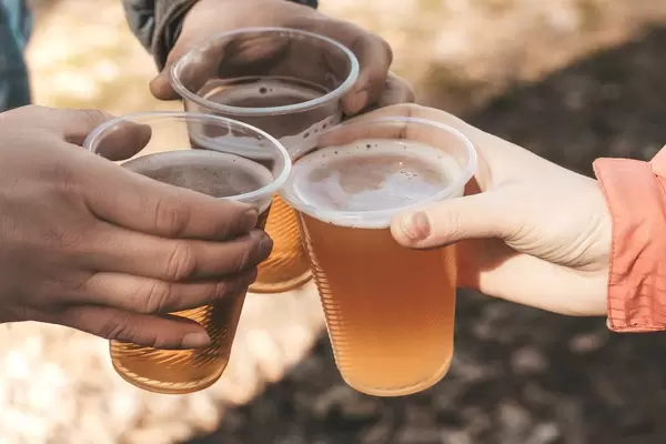 Three hands holding plastic beer glasses on spring nature background