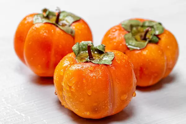 Three ripe orange persimmons on a white wooden background (Flip 2019)