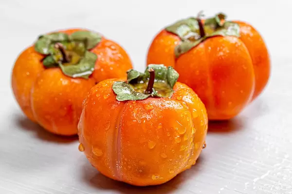 Three ripe orange persimmons on a white wooden background