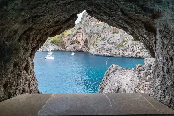 Three sailboats in the blue waters of the sea framed in a window made of rocks at Sa Calobra, Majorca