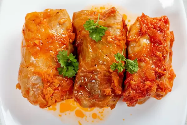 Three stuffed cabbage rolls in tomato sauce on a white plate (Flip 2019)