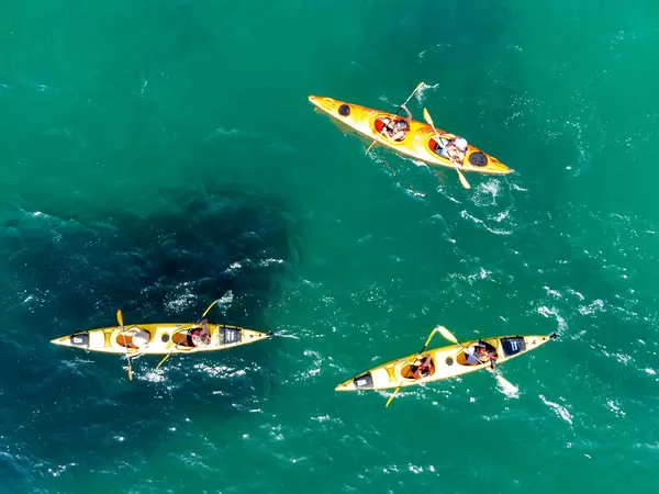 Three yellow kayaks with two people each on board in the waters of Kastani Beach at Skopelos. Drone photo