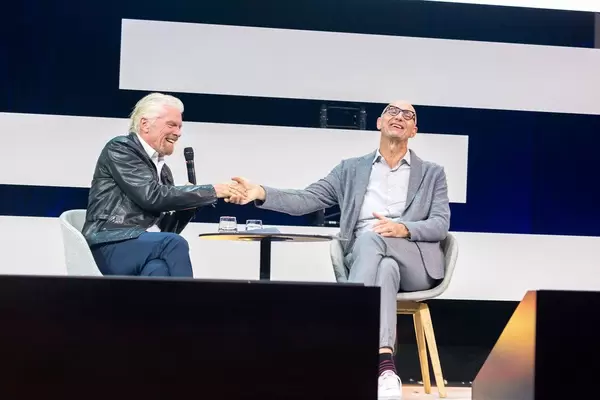 Tim Höttges und Richard Branson geben sich die Hand und Lachen dabei