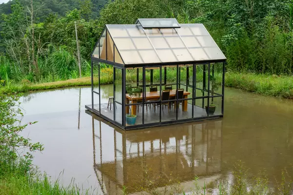Tisch und Stühle in einem Glashaus in der Mitte eines Teiches in der Natur