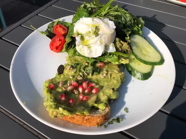 Toast mit Avocado, Granatapfelkernen und Kräutern, mit Gurken, Salat und Cherry-tomaten serviert
