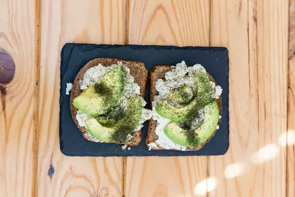 Toastbrot mit Ricotta und Avocado mit Steinplatte auf Holztisch