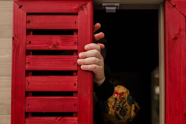 Toddler Playing With Red Window In Wooden House