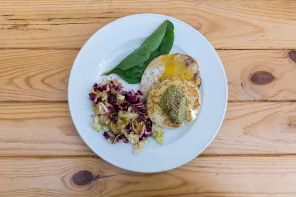 Tofu Burger aus weissen Bohnen serviert mit Salat und Spinat auf Holztisch