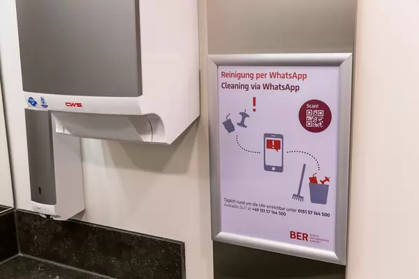 Toilette vom Flughafen BER in Berlin: Schild mit Hinweis "Reinigung per Whatsapp" und QR Code