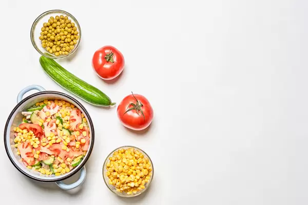 Tomaten, Gurke, Topf und Schalen mit Mais und Erbsen auf weißem Hintergrund mit Platz für Text