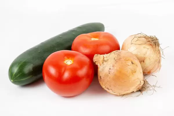 Tomaten, Gurke und zwei Zwiebeln mit Schale vor weißem Hintergrund