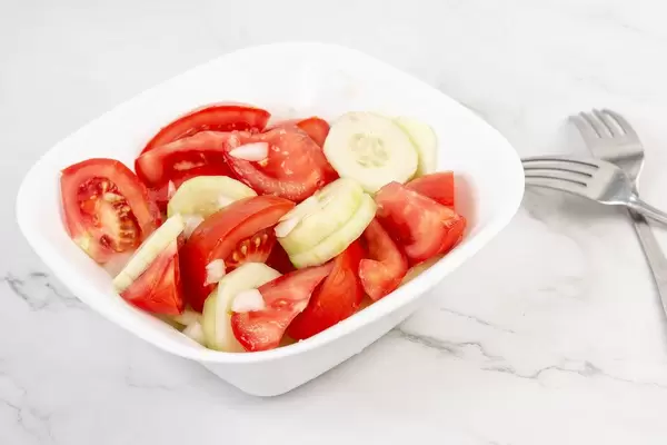 Tomaten-Gurken-Zwiebel-Salat in einer kleinen Salatschüssel neben zwei Gabeln