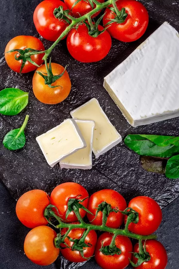 Tomatenstränge und Schimmelkäse mit Basilikum auf schwarzer Schieferplatte von oben fotografiert