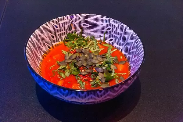 Tomato, carrot and celery soup topped by herbs and seeds in a black and white bowl on black background