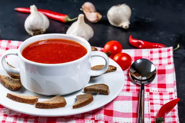 Tomato soup in a tureen with croutons, garlic, chili and a spoon on the table