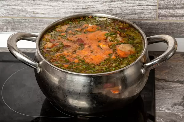 Tomato soup with sorrel and dill is being cooked in a saucepan on an electric hob