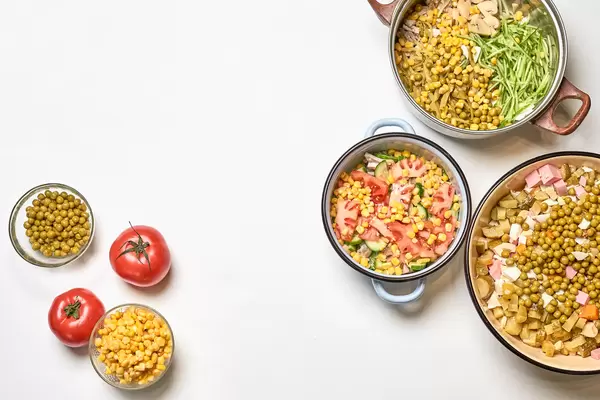 Tomatoes, pots and two small bowls with sweetcorn and peas on white background with copy space