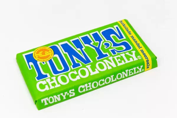 Tony's Chocolonely chocolate bar with almonds and sea salt in a green package on white background: 100% slave free
