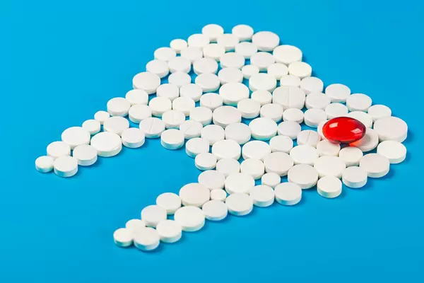 Tooth made of white pills with one red capsule on blue background
