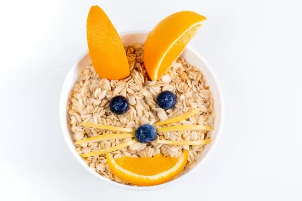 Top view, a bowl of oatmeal decorated with fresh fruit in the shape of a rabbit face