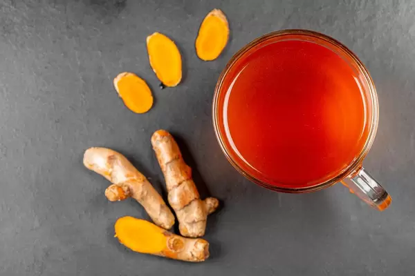 Top view, a cup of tea with fresh turmeric root and slices on a black background (Flip 2020)