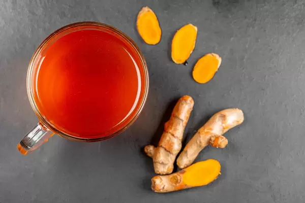 Top view, a cup of tea with fresh turmeric root and slices on a black background
