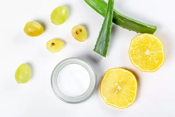 Top view, a jar of cream on a white background with fresh grapes, lemon slices and aloe