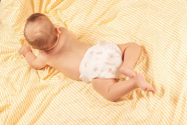 Top view, a small baby in diapers lies on his stomach