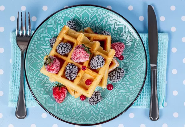 Top view, Belgian waffles with strawberries, red currants and blackberries on a blue background