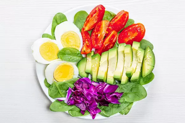 Top view boiled eggs with spinach, avocado, purple cabbage and tomatoes