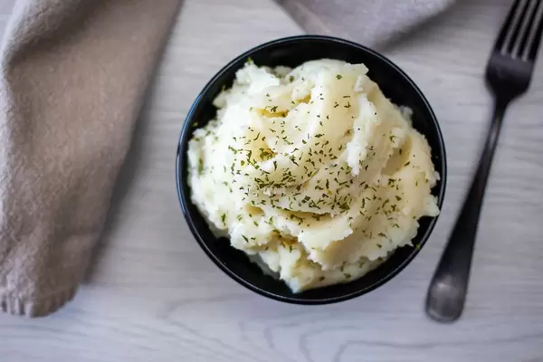 Top View Bokeh Food Photo of Masked Potatoes in a Black Ceramic Bowl next to a Form on a Wooden Table