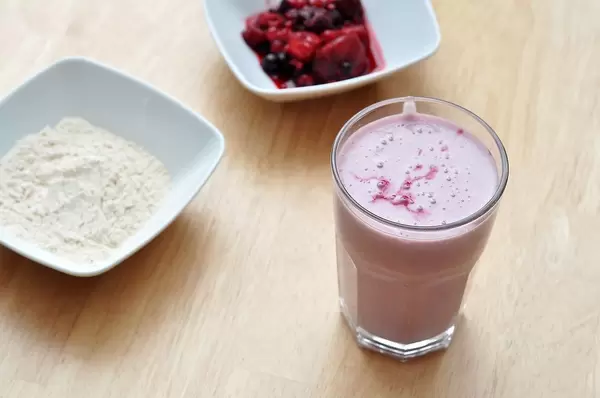 Top View Bokeh Photo of Protein Berry Shake in Glass next to Bowl with Protein Powder and Fresh Berries on Wooden Table