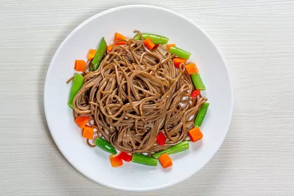 Top view buckwheat noodles with asparagus, carrots and sweet peppers on a white wooden background