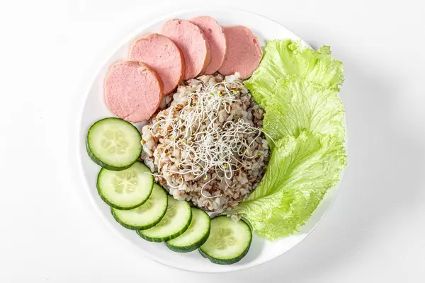 Top view buckwheat porridge with sausage, lettuce, cucumber and alfalfa micro greenery on white background (Flip 2019)