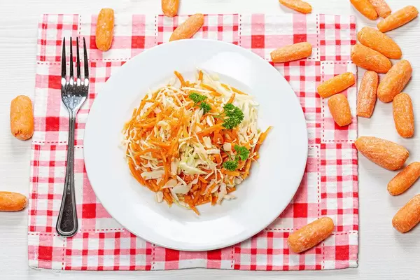 Top view carrot and cabbage salad on a plate surrounded by a small fresh carrot (Flip 2019)