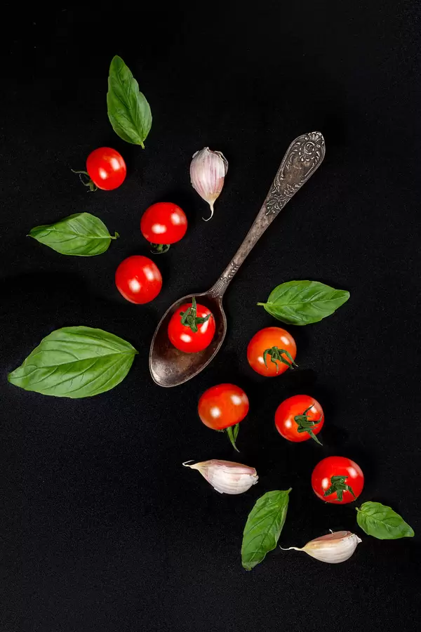 Top view, cherry tomatoes, garlic and basil leaves on a black background