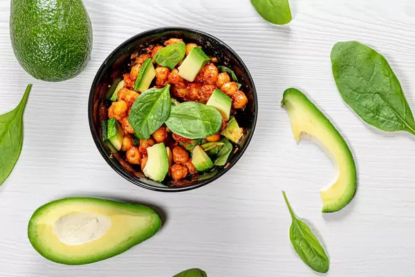 Top view chickpeas in tomato sauce with fresh avocado and spinach on white wooden background (Flip 2019)