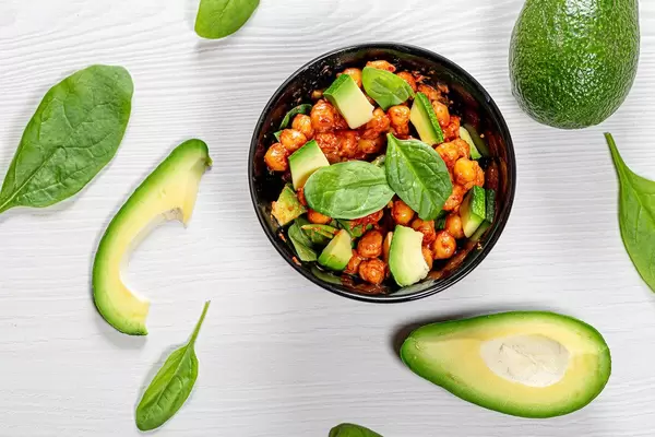 Top view chickpeas in tomato sauce with fresh avocado and spinach on white wooden background