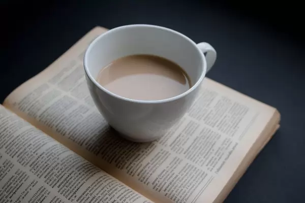 Top View Close Up Photo of Cup of Coffee standing on open Book on Black Table