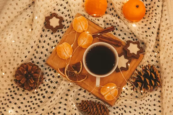 Top view, cup of coffee with cookies, tangerines, garland and pine cones