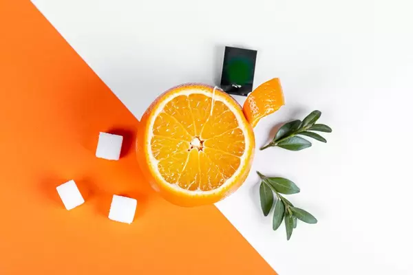 Top view, cup of orange with sugar and green leaves on white-orange background