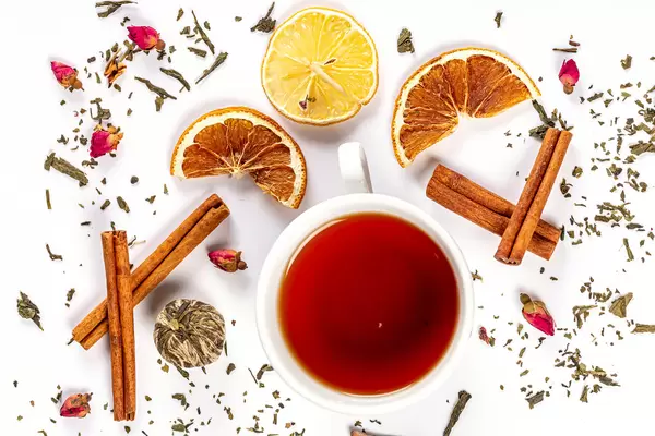 Top view, cup of tea on white background with cinnamon, dried lemons and flowers