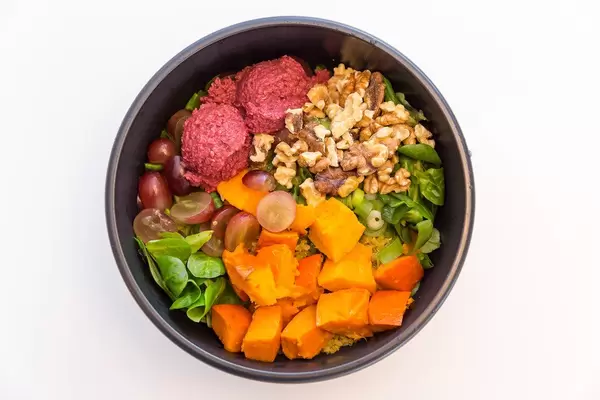 Top view der Vegetarischen Erntedank Bowl mit Hummus aus roter Beete, Feldsalat, warmer Curry Quinoa, gerösteter Hokkiado Kürbis, rote Trauben, jungem Lauch, Walnusskernen und Joghurt-Orangen-Dip