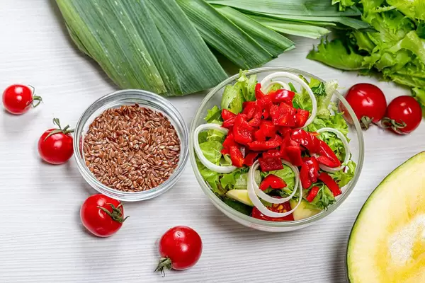 Top view dietary vegetable salad in glass bowl with ingredients on white wooden background