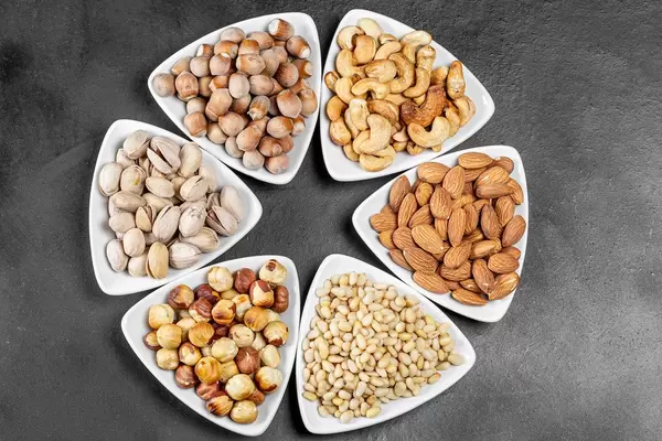Top view, different nuts in white triangular bowls on a black background (Flip 2020)