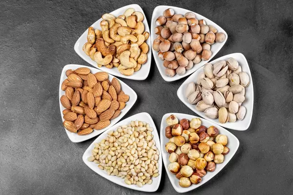 Top view, different nuts in white triangular bowls on a black background